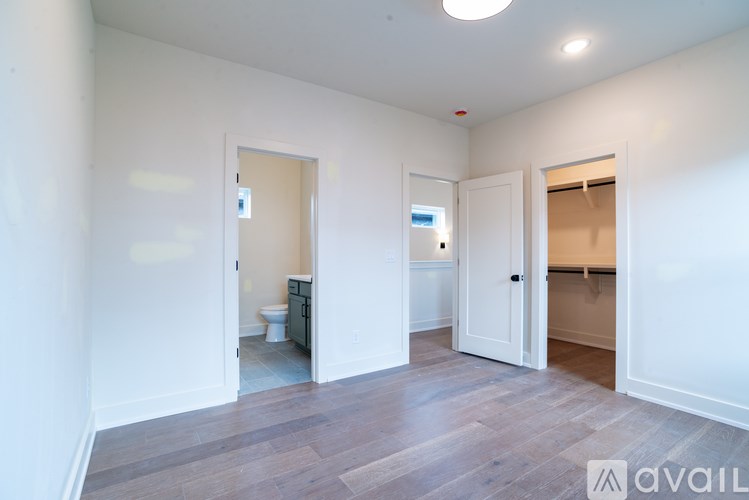 A room with a wooden floor and white walls, with a toilet visible through an open door.