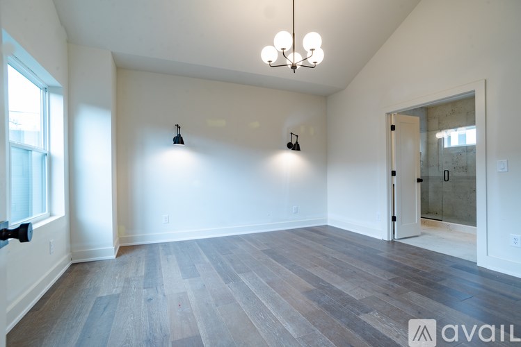 A spacious room with a chandelier, two wall sconces, and a door leading to a bathroom.