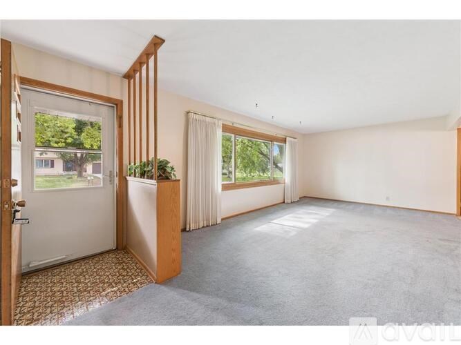 A room with a carpeted floor, a wooden cabinet, and a large window with a view of trees.