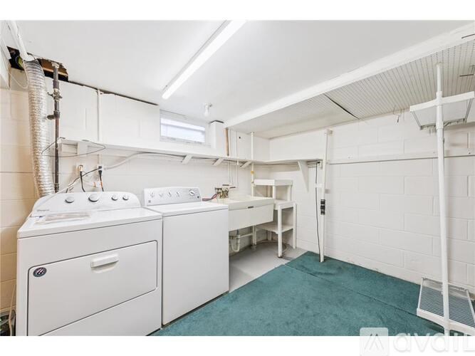 A laundry room with a washer and dryer, ironing board, and a green rug.