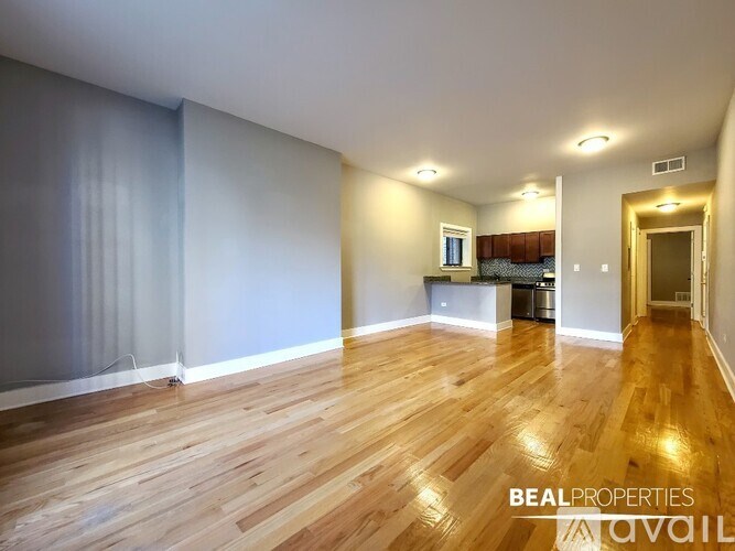 A spacious room with wooden flooring and a large window with curtains.