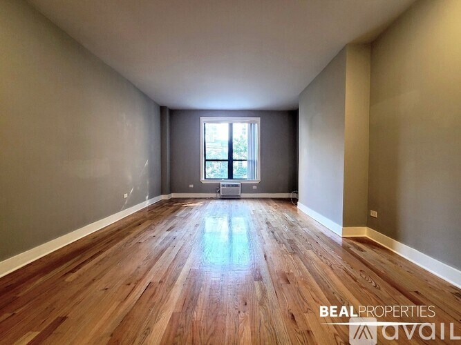 A spacious room with wooden flooring and a window in the middle.