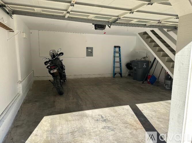 A motorcycle is parked in a garage with a ladder and a trash can.