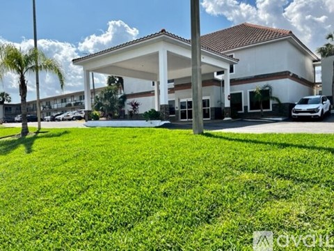 A white building with a red roof is surrounded by a green lawn.