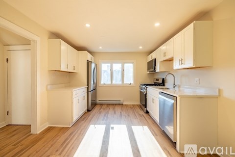 A kitchen with white cabinets and appliances, a window, and wooden flooring.
