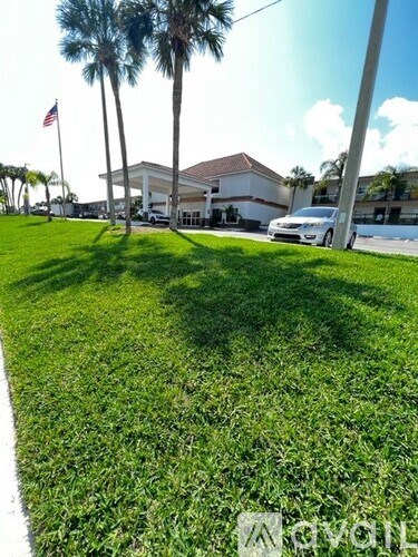 A white car is parked in front of a house with a flag on a pole.