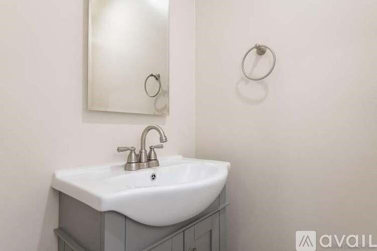 A white sink with a silver faucet is mounted on a grey cabinet.
