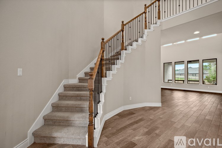 A wooden staircase with a carpeted runner leads up to a bright room with a large window.