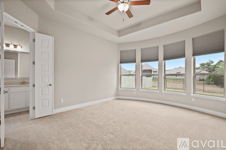 A room with a carpeted floor, a ceiling fan, and a view of the outdoors through the windows.