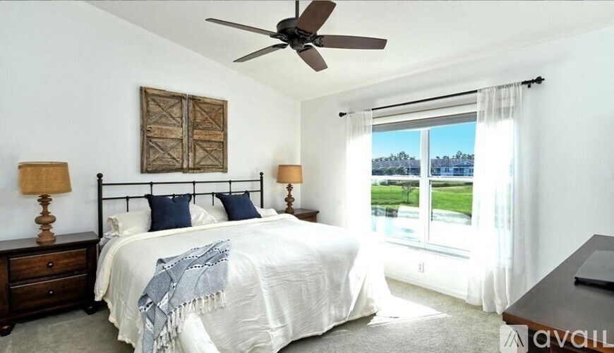 A bedroom with a large bed, a ceiling fan, and a view of the outside through a window.