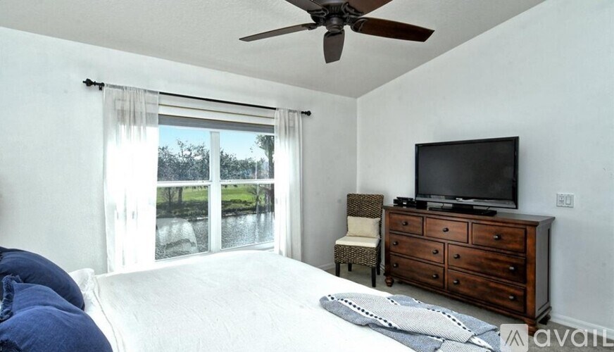 A bedroom with a bed, a dresser with a television, and a window with a view of a lake.