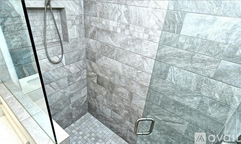 A shower with a glass door and grey tiles.