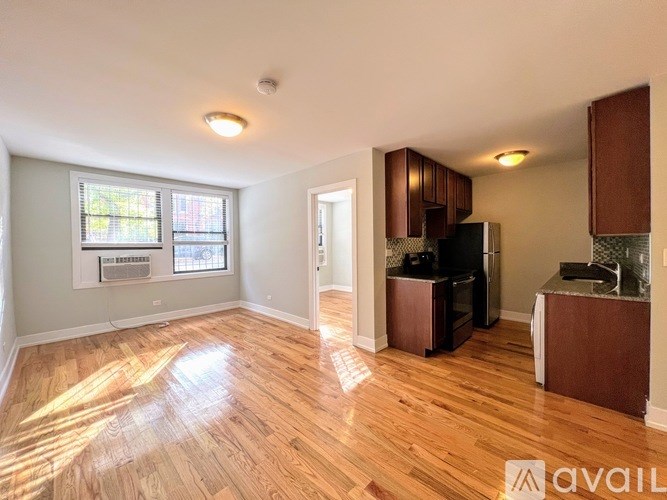 A living room with wooden floors and a kitchen area in the background.