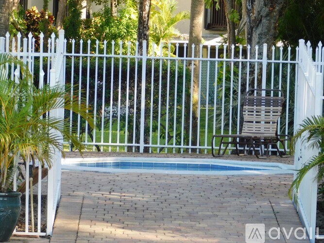 A white fence surrounds a pool area with a chair and potted plants.