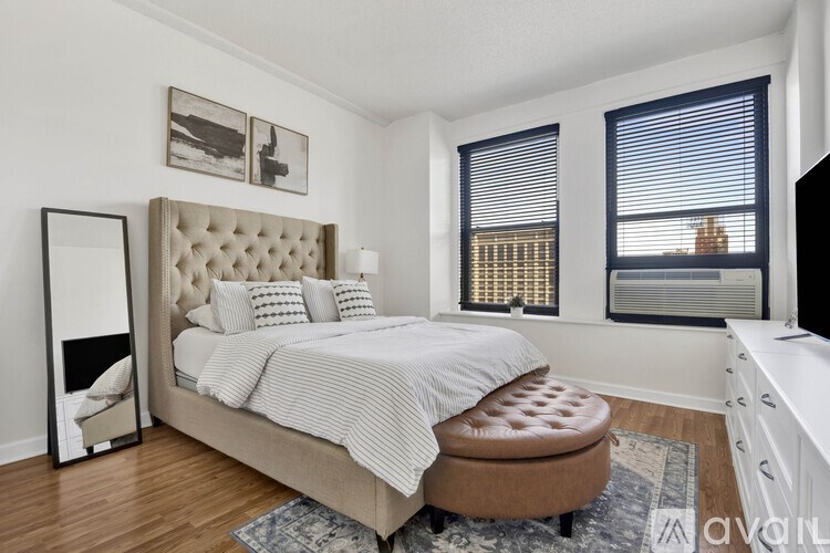 A bedroom with a large bed and a brown ottoman.
