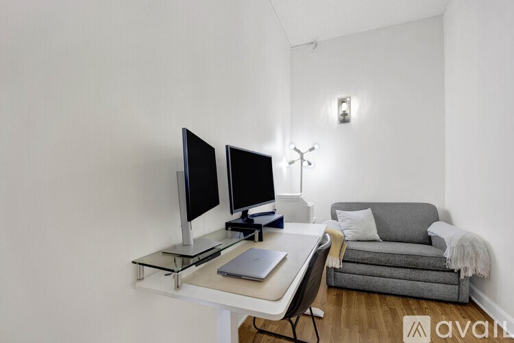 A modern home office with a laptop, two monitors, and a couch.