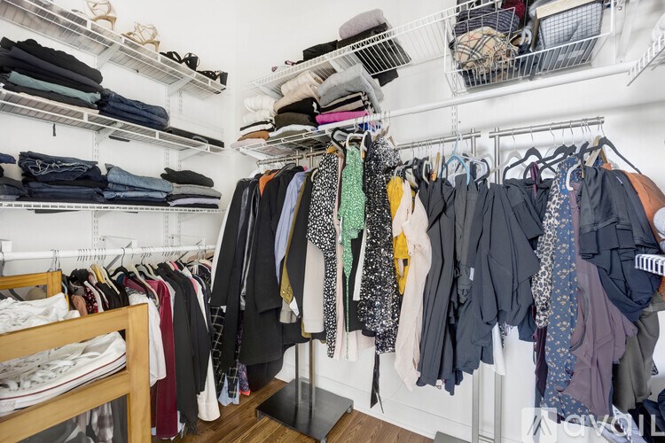 A white closet with clothes hanging on hangers.