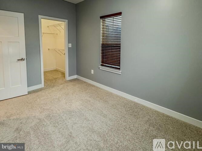 A room with a carpeted floor, a door, and a window with blinds.