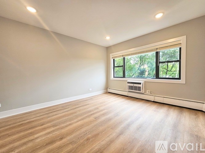 A spacious room with wooden flooring and a large window.