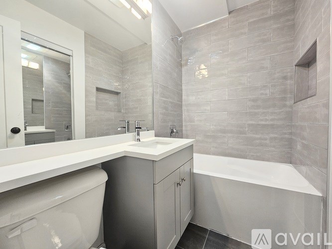 A bathroom with a white countertop and a grey tiled wall.