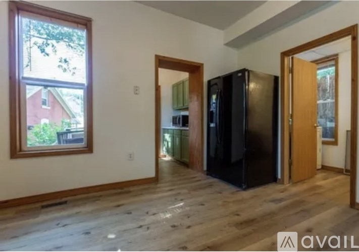 A kitchen area with a black fridge, a window, and wooden flooring.