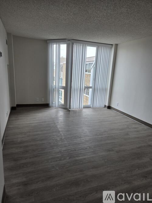 A room with wooden flooring and a large window with blinds.
