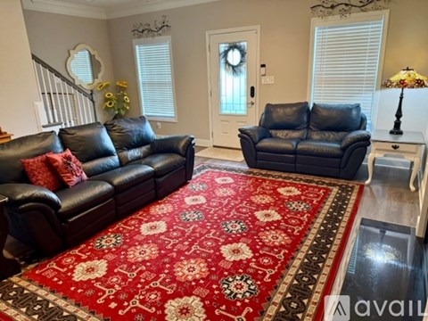 A living room with a red rug and two black leather sofas.