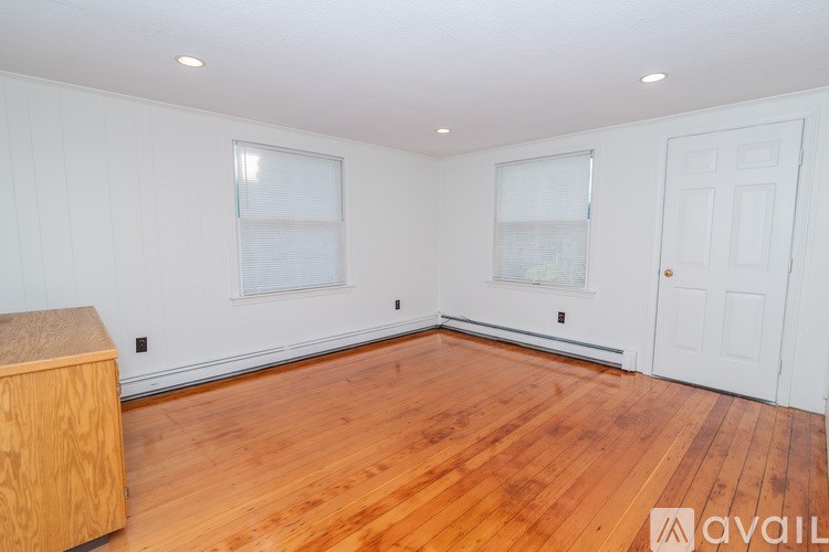 A room with wooden floors and white walls, with a wooden cabinet on the left and a door on the right.