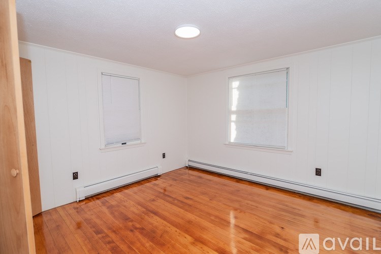 A room with wooden floors and white walls, with a window and a door on the right side.