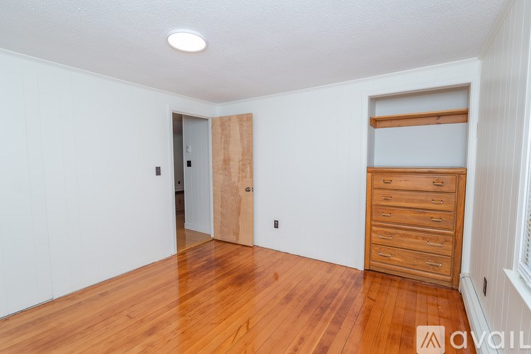 A room with wooden floors and a white wall with a door and a drawer unit.