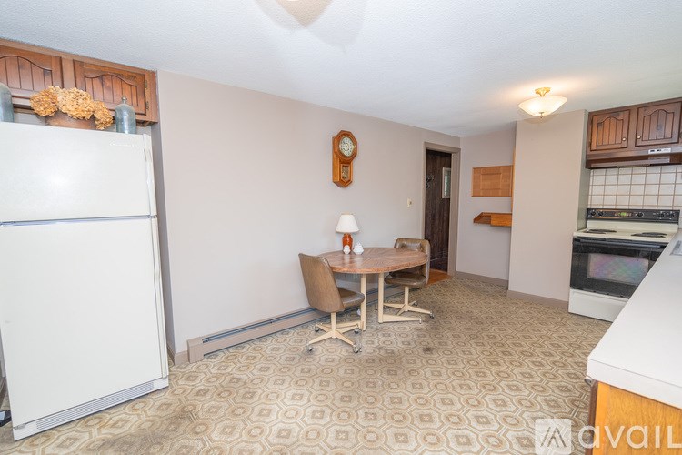 A kitchen with a white refrigerator, a table with chairs, and a clock on the wall.