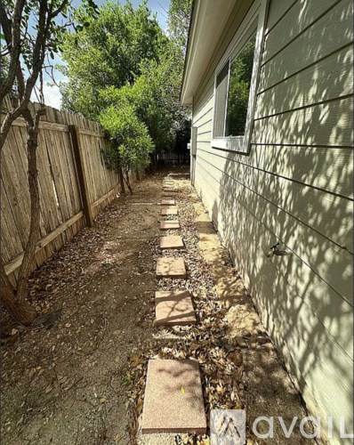 A narrow pathway with stepping stones runs between a wooden fence and a house.