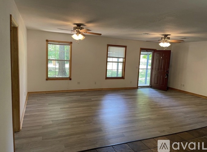 A spacious room with wooden flooring and two windows.