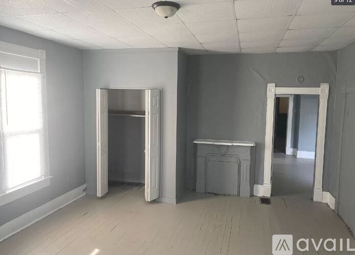 A room with a white ceiling, a window on the left, a door on the right, and a table in the middle.