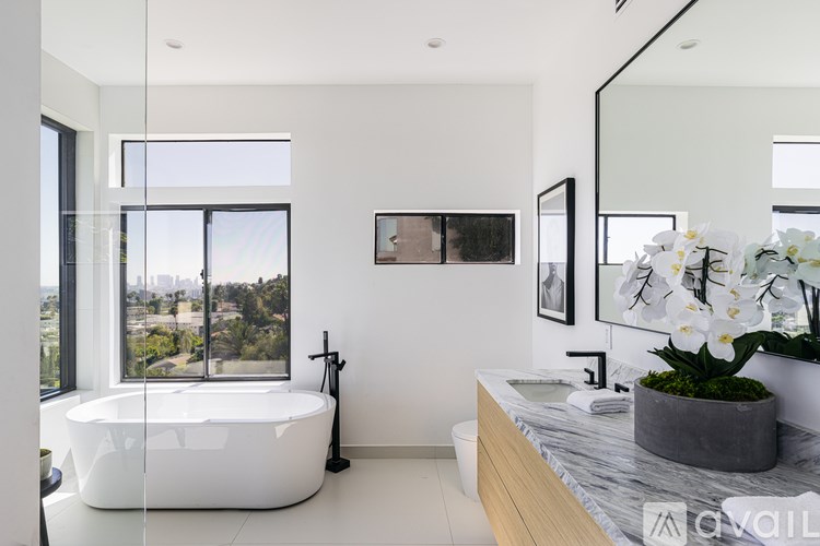 A modern bathroom with a large window, a white bathtub, and a marble countertop.
