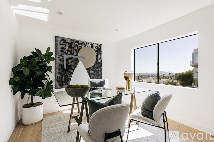 A modern living room with a glass table and chairs, a potted plant, and a large abstract painting on the wall.
