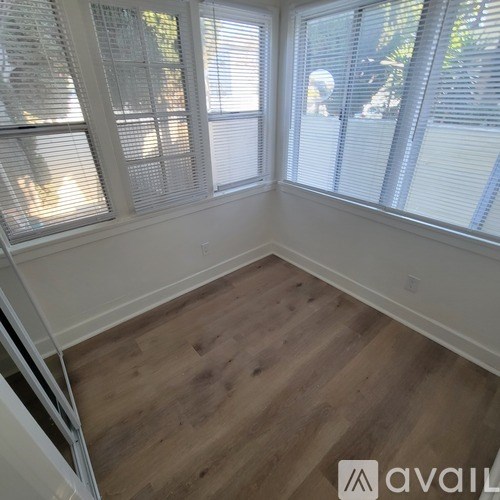 A room with wooden flooring and three windows covered with blinds.