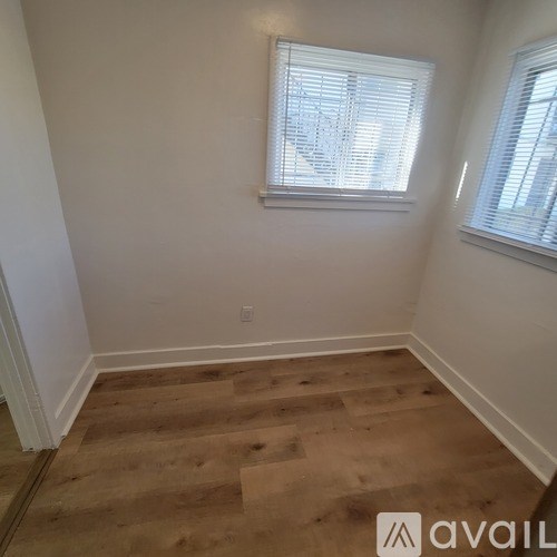 A room with wooden flooring and two windows.