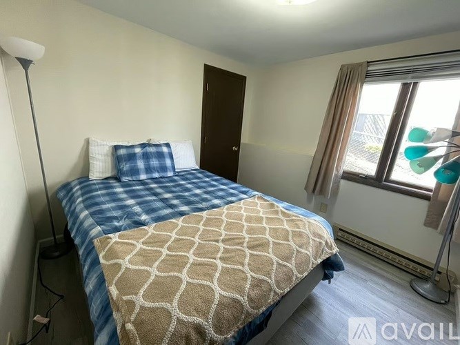 A bedroom with a bed covered in a blue and beige patterned blanket.