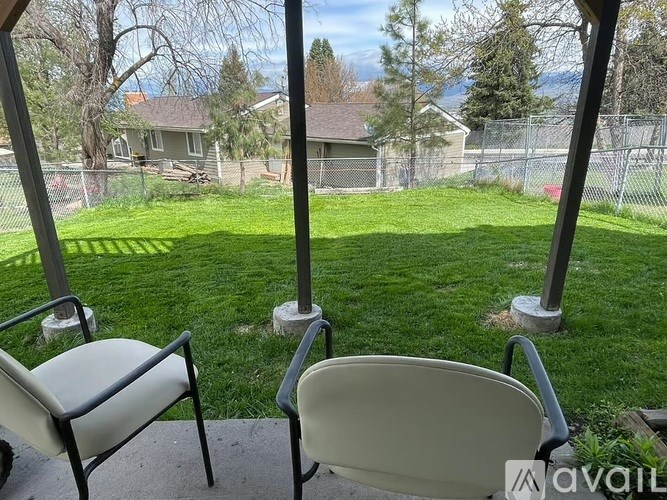 Two chairs are on a porch with a view of a fenced yard and houses.