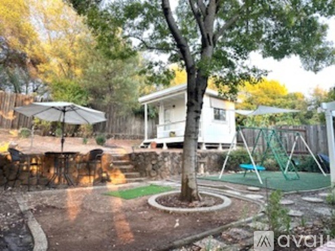 A backyard with a tree, a swing set, and a patio umbrella.