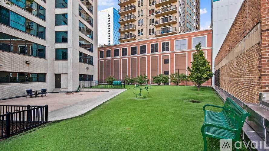 A grassy area with a bench and a tree in the middle of a courtyard surrounded by buildings.