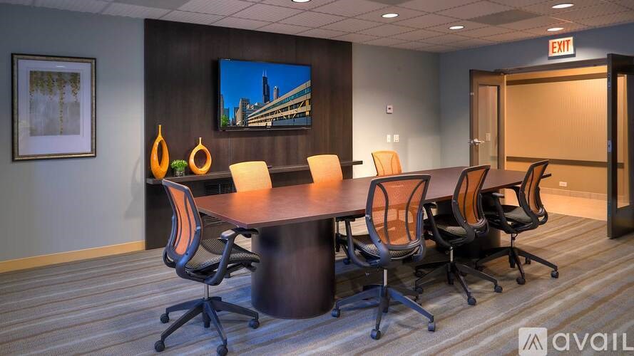 A conference room with a large table and chairs, a television on the wall, and a framed picture.