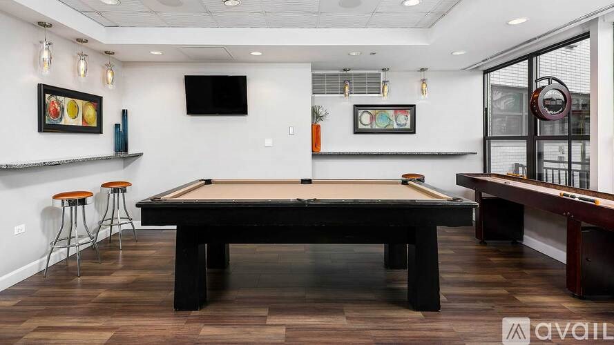 A pool table is in the middle of a room with a TV and a bar.