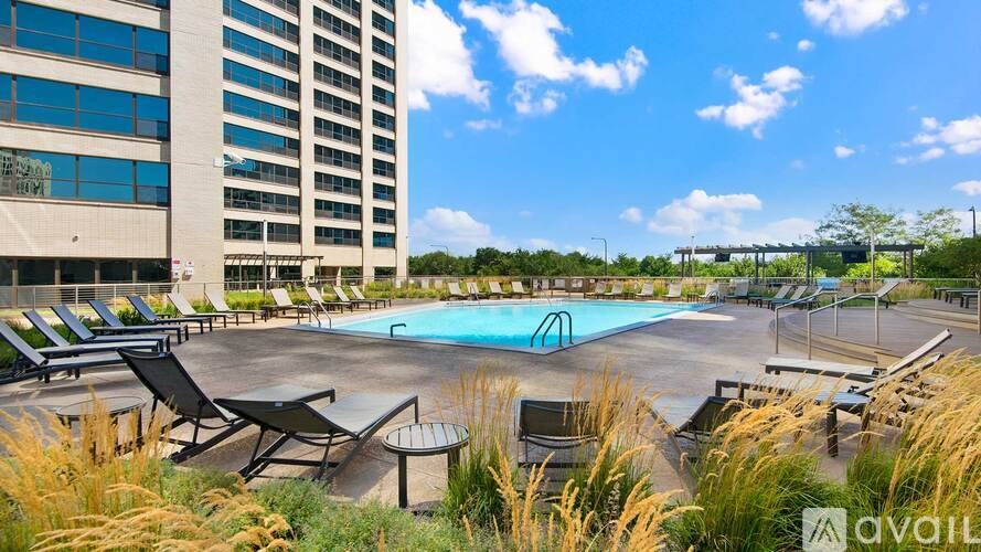 A pool surrounded by chairs and tall grasses with a building in the background.