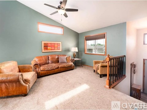 A living room with a brown leather couch and a ceiling fan.