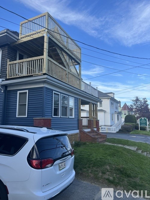 A white car is parked in front of a blue house with a balcony.