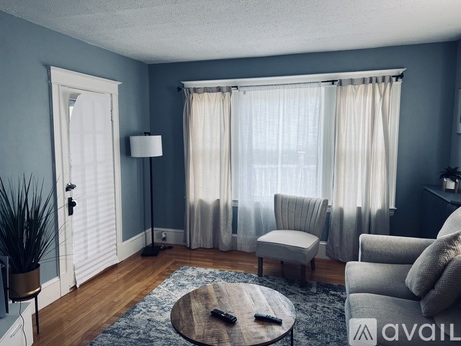 A living room with a grey couch, a wooden coffee table, and a window with curtains.