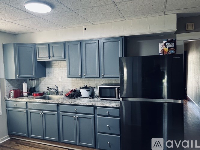 A kitchen with a black refrigerator and grey cabinets.