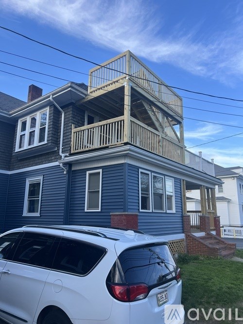 A white car is parked in front of a blue house.